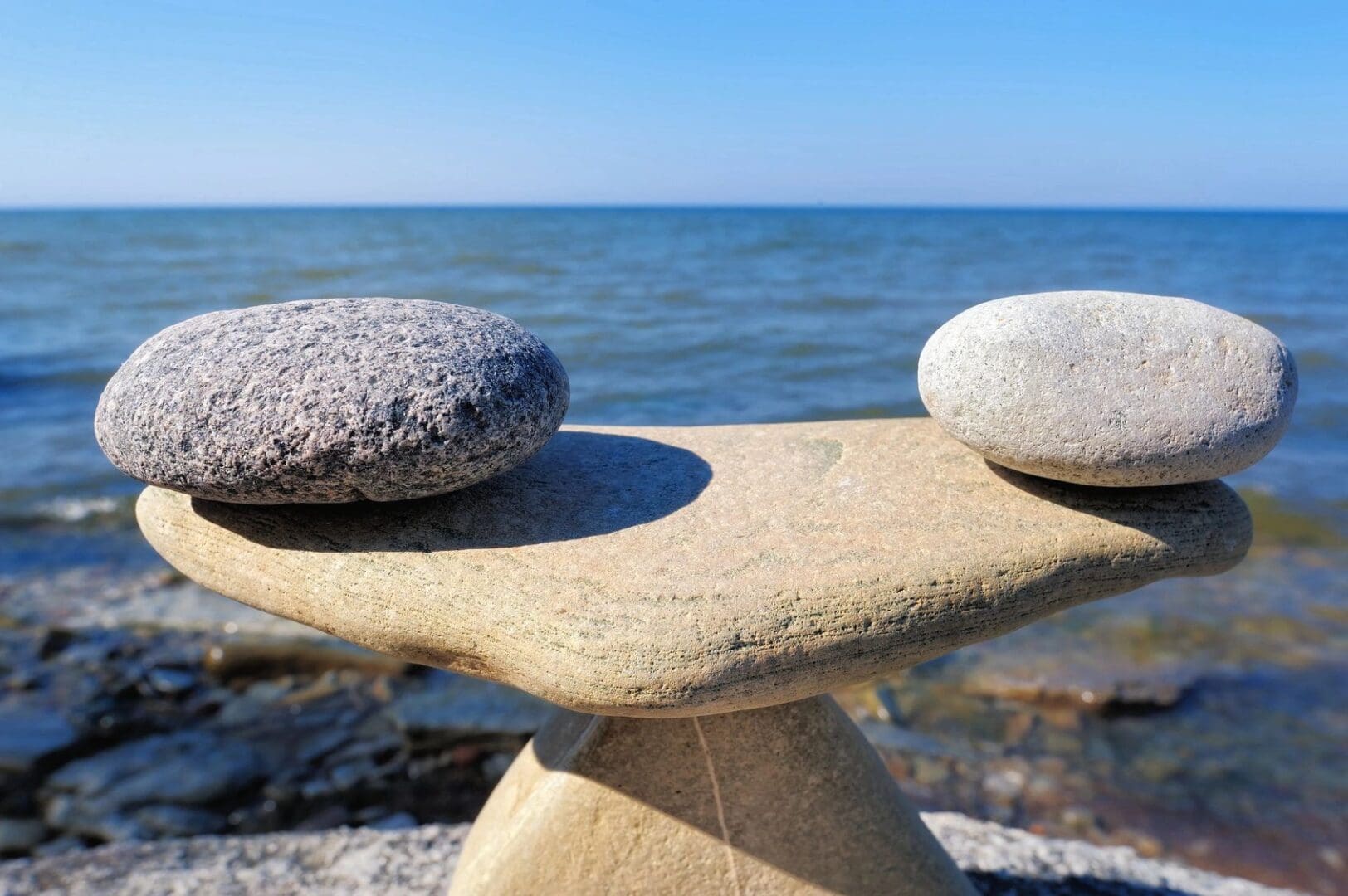 Two stones are sitting on a table near the ocean.