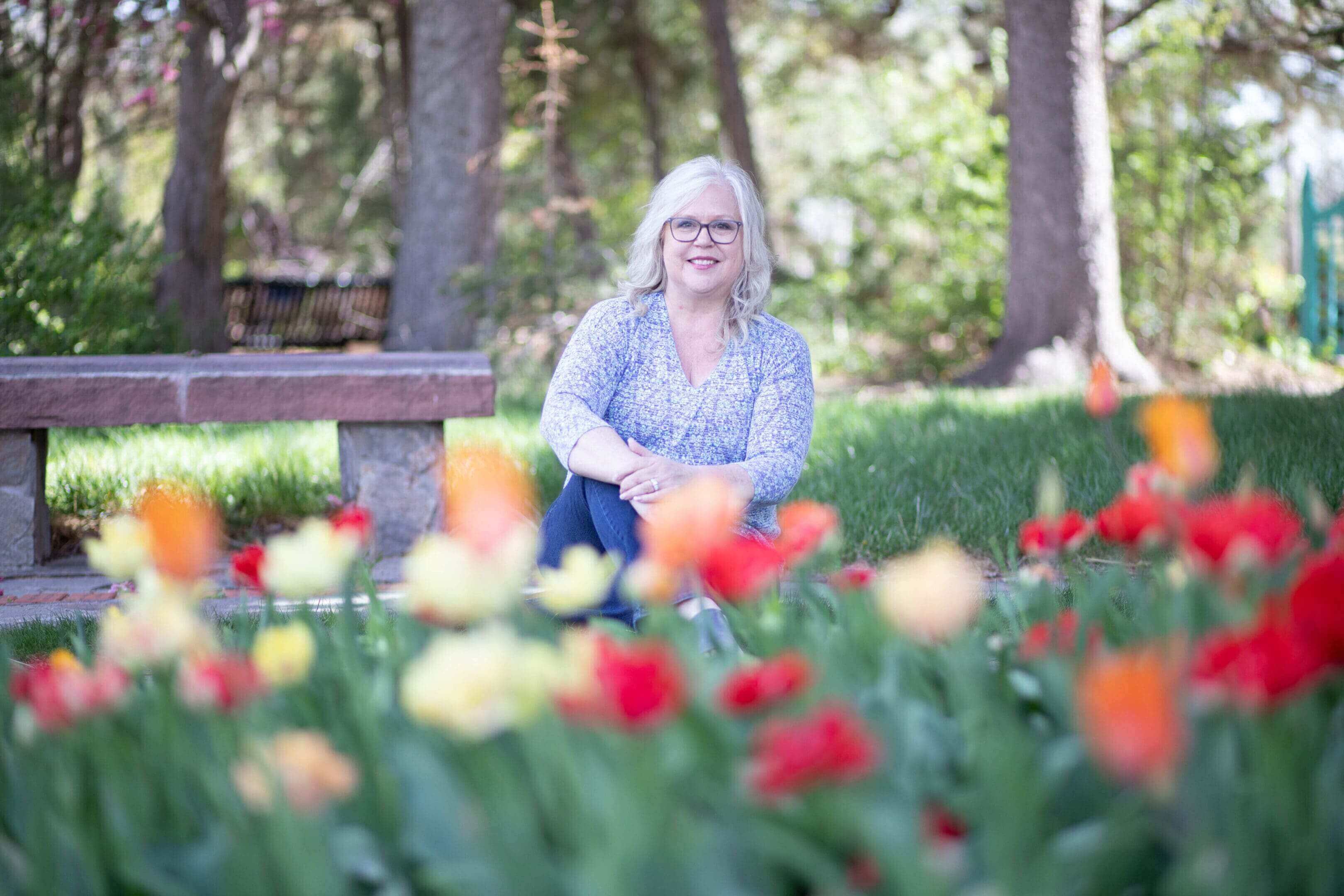 A woman sitting on the ground in front of some flowers.