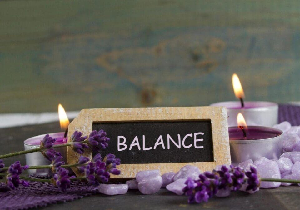 A sign that says balance with candles and flowers around it.